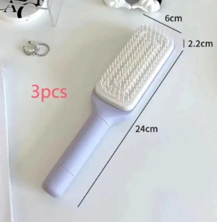 hairbrush with a white and blue color scheme, held in a person's hand, with a round pad and detangling bristles visible.